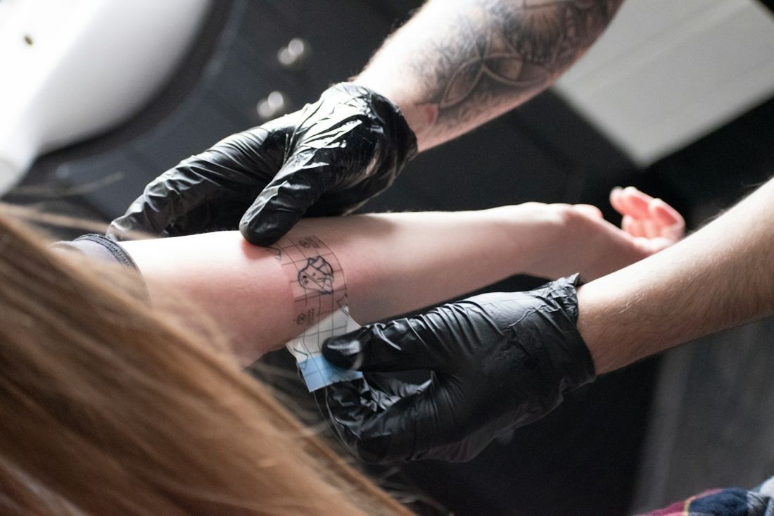 Tattoo artist in black gloves placing a stencil on a client's forearm