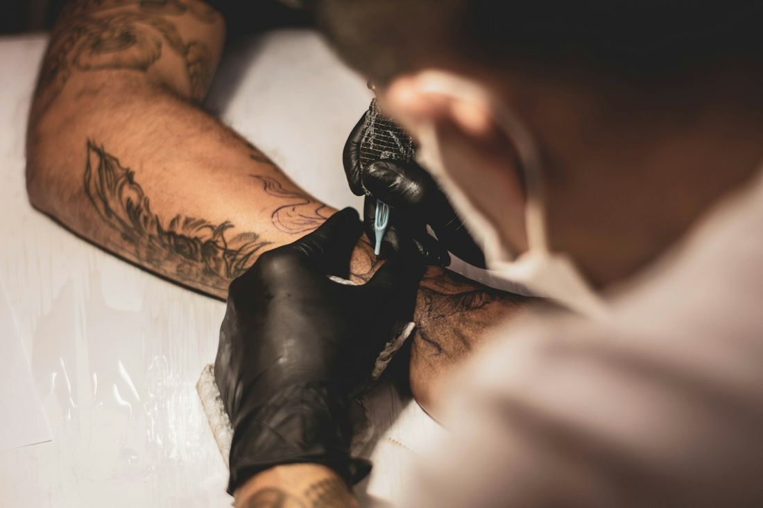 Tattoo artist in black gloves tattooing a client's arm