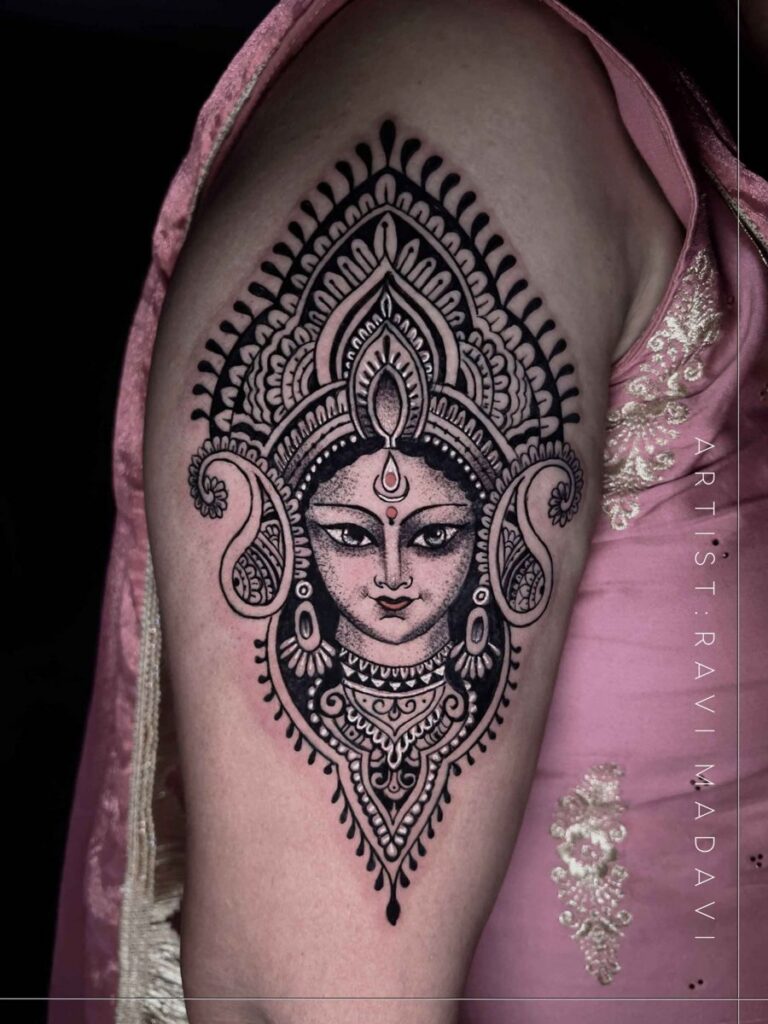 Goddess Durga face framed by an ornamental mandala tattoo on the upper arm